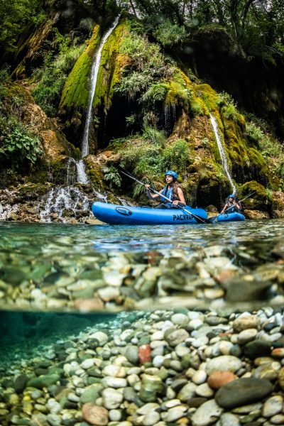 Two women paddling bright inflatable packrafts through the green waters of the Tara River Canyon in Montenegro.